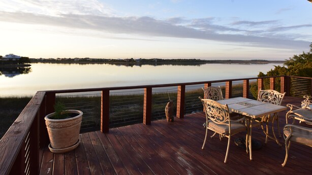 A wooden deck with outdoor furniture overlooking a calm lake. - WATERFRONT Home  - Dolphins, Sunsets, Fishing, Kayaks, Canoe, Wildlife (Crawfordville)