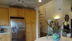 A kitchen with wooden cabinets, a stainless steel refrigerator, a ceiling fan, and a decorative vase on the countertop. - WATERFRONT Home  - Dolphins, Sunsets, Fishing, Kayaks, Canoe, Wildlife (Crawfordville)