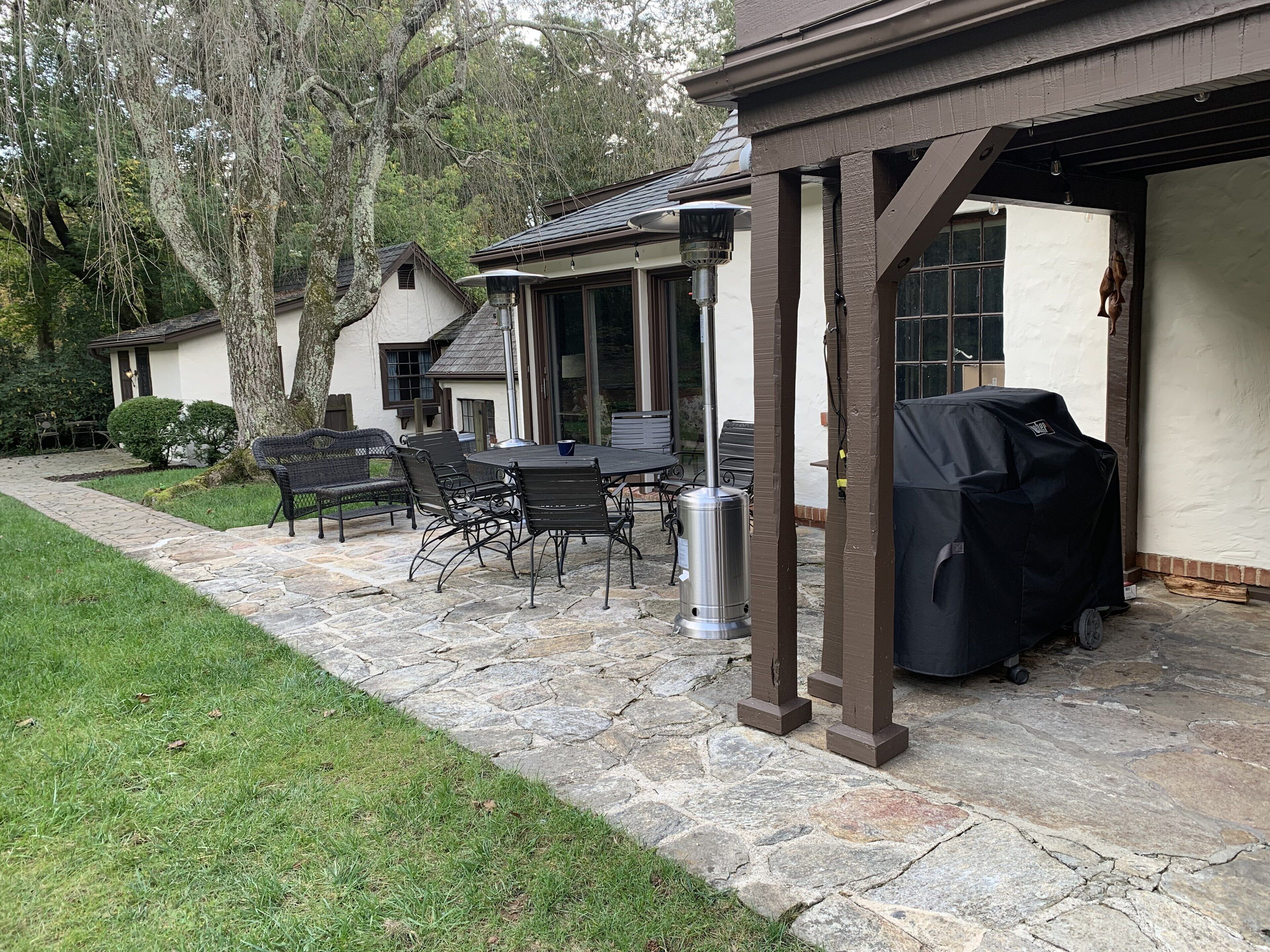 Eine Terrasse mit Steinböden, Gartenmöbeln und einem Grill.