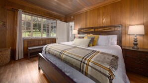 Camera da letto con rivestimento in legno, un letto grande, una panca, una finestra e una ventola a soffitto.