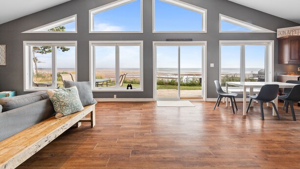 A spacious living area with a large window, a wooden bench, and a dining table with chairs. - Beachfront Chalet (Stratford)