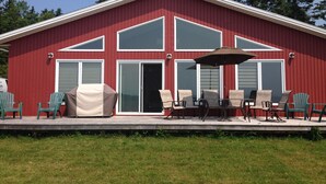 A red building with a covered patio area featuring outdoor furniture and a large umbrella. - Beachfront Chalet (Stratford)