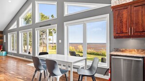 A modern kitchen with large windows, a dining area with a white table and chairs, and wooden flooring. - Beachfront Chalet (Stratford)