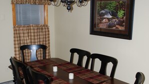 Un comedor con una mesa de madera, seis sillas, una araña, un cuadro en la pared y una ventana con persianas.