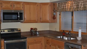 Una cocina con armarios de madera, microondas, estufa, lavavajillas y una ventana con persianas.