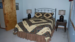 Un dormitorio con una cama, dos mesitas de noche con lámparas, una puerta de madera y un estante en la pared.