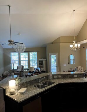 A spacious kitchen with a granite countertop, a built-in sink, and a ceiling fan. There are large windows providing natural light and a view of the outdoors. - Masters rental 0.95miles from course (Augusta)