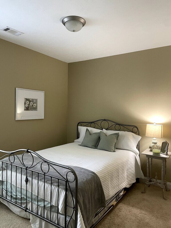 A bedroom with a metal bed frame, a bedside table with a lamp, and a framed picture on the wall. - Masters rental 0.95miles from course (Augusta)