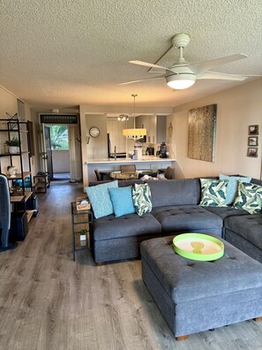 A modern living room with a grey sectional sofa, a coffee table, and a ceiling fan. - Unbeatable Location at Kamaole III Beach - Kam Sands Bldg. 1 (Kihei)