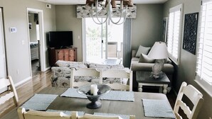 A dining area with a table set for four, a chandelier, and a television in the background. - Pet-Friendly,No Cleaning Fees, 2BR/2BA Condo Near Pool in Bethany Bay - Sleeps 6 (Ocean View)