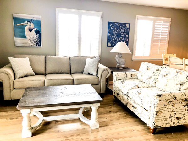 A living room with a beige sofa, a patterned sofa, a coffee table, and a lamp. - Pet-Friendly,No Cleaning Fees, 2BR/2BA Condo Near Pool in Bethany Bay - Sleeps 6 (Ocean View)