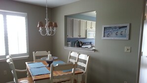 A dining area with a wooden table, white chairs, a chandelier, and a kitchen in the background. - Pet-Friendly,No Cleaning Fees, 2BR/2BA Condo Near Pool in Bethany Bay - Sleeps 6 (Ocean View)