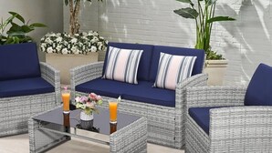 Un ensemble de meubles de jardin en osier avec des coussins, une table basse en verre avec des boissons et un arrangement floral.