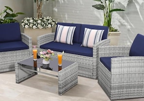 A wicker sofa set with cushions, a glass coffee table with drinks, and a floral arrangement.