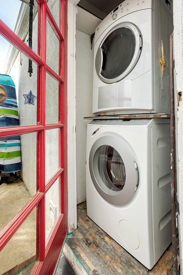 A laundry room with stacked washing machines and a red-framed window.