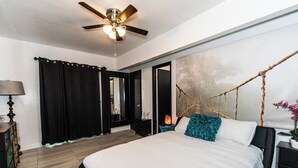 Une chambre à coucher comprenant un lit, un ventilateur de plafond, une table de chevet, une lampe et une œuvre d’art accrochée au mur.