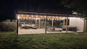 Un espace extérieur aménagé en terrasse, doté d’un coin salon couvert, d’un jacuzzi et d’un barbecue.