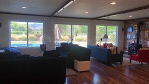 Un salon spacieux avec une grande fenêtre, une cheminée et une piscine visible à l’extérieur.
