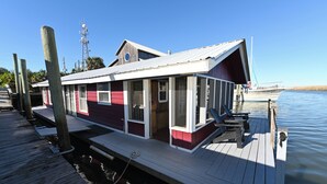 Una casa flotante amarrada con cubierta, ventanas y un pequeño porche.
