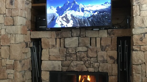 A stone fireplace with a flat-screen TV mounted above it, displaying a mountain scene.