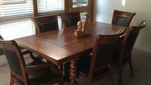 A wooden dining table with six chairs, a decorative deer figurine, and a window with blinds.