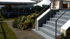 A building with a staircase leading to a porch, surrounded by a garden with various plants.