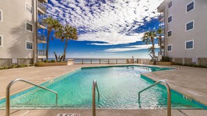 Relax by the ocean-view pool surrounded by a wooden deck and two-story buildings with balconies.