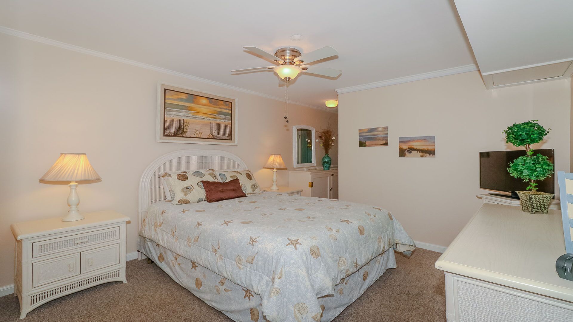 A bedroom with a bed, two bedside tables, a ceiling fan, a dresser, a TV, and wall art.