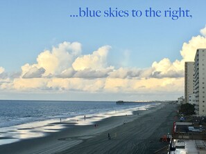 Une plage avec une jetée qui s’avance dans la mer, des bâtiments le long de la côte et un ciel dégagé.
