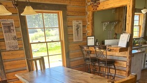A rustic wooden dining area with a large table and chairs, a kitchen area with a sink and counter, and a view of the outdoors through a window.