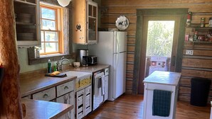 A rustic kitchen with wooden cabinets, a white refrigerator, and a sink with a window above it.