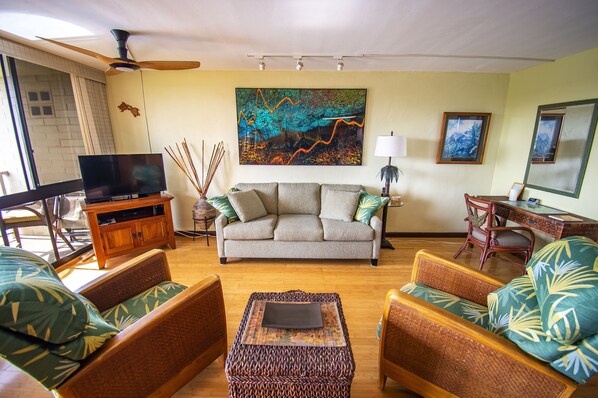 A living room with a sofa, armchairs, a coffee table, a TV, and artwork on the walls. - Kauai Oceanfront, Poipu 'Jewel on the Sea', AC, swimmable beaches, Kuhio Shores (Koloa)