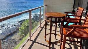 A balcony with a view of the ocean, featuring a round wooden table and two wooden chairs.