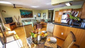 A spacious living area with a dining table, chairs, a TV, and a kitchen area with wooden cabinets and a refrigerator.