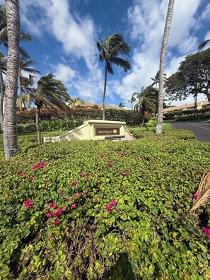 A landscaped area with a sign reading 'Maui Kamaole' surrounded by lush greenery and palm trees.
