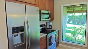 Une cuisine moderne dotée d’appareils électroménagers en acier inoxydable, de meubles en bois et d’une grande fenêtre donnant sur un paysage verdoyant.