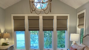 A bedroom with a large bed, a chandelier, and windows with blinds. - Luxurious Lakefront Retreat (Northport)