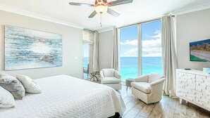 Ein Hotelzimmer mit einem großen Bett, zwei Sesseln, einem Schreibtisch und Blick aufs Meer.