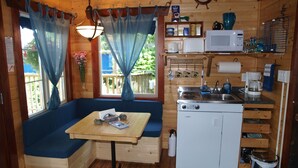Eine kleine Küche mit Herd, Mikrowelle und Spüle. Ein Holztisch mit einer Bank und ein Fenster mit Vorhängen.