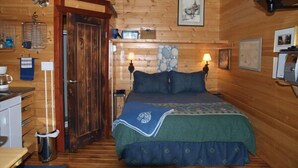 Ein gemütliches Schlafzimmer in einer Blockhütte mit Holzbalkendecke, einem Bett mit blaugrüner Bettdecke, einem kleinen Nachttisch und einer Wandlampe.