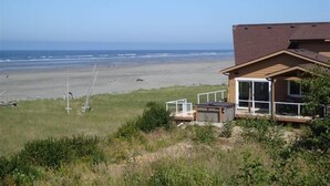 Ett hus vid stranden med en stor glasdörr, en veranda och utsikt över havet.