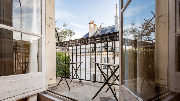 En balkon med gelænder, to små borde og udsigt til en bygning med skorsten.