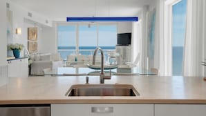 A modern kitchen with a large window, a dining area with a view of the sea, and a TV mounted on the wall.