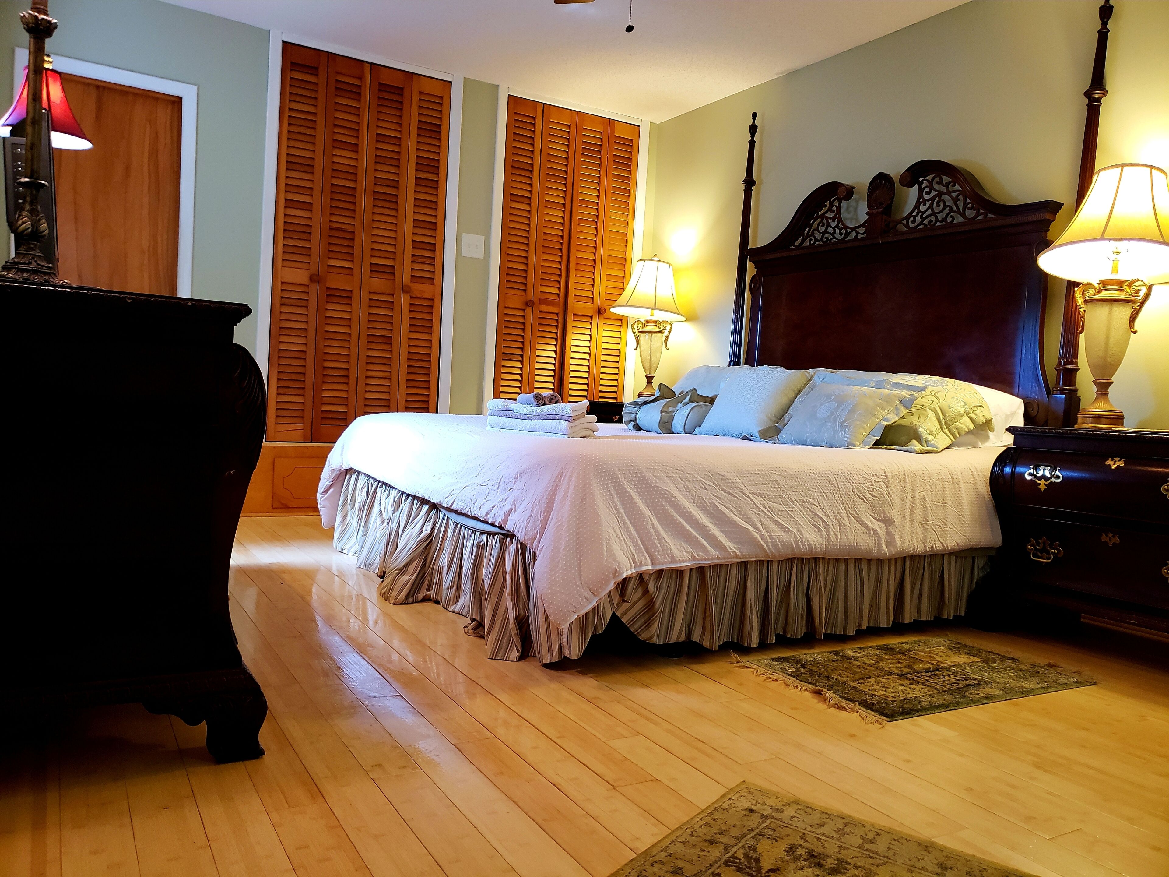 Une chambre à coucher avec un grand lit, une tête de lit en bois, deux lampes de chevet et une commode en bois.