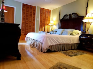 Une chambre à coucher avec un grand lit, une tête de lit en bois, deux lampes de chevet et une commode en bois.