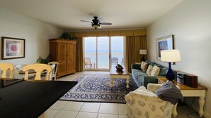 A living room with a sofa, chairs, a coffee table, a cabinet, and a balcony with a view.