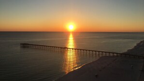 A sunset over a beach with a pier extending into the water.