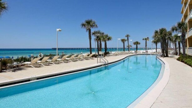 A swimming pool with lounge chairs and palm trees, overlooking the ocean.