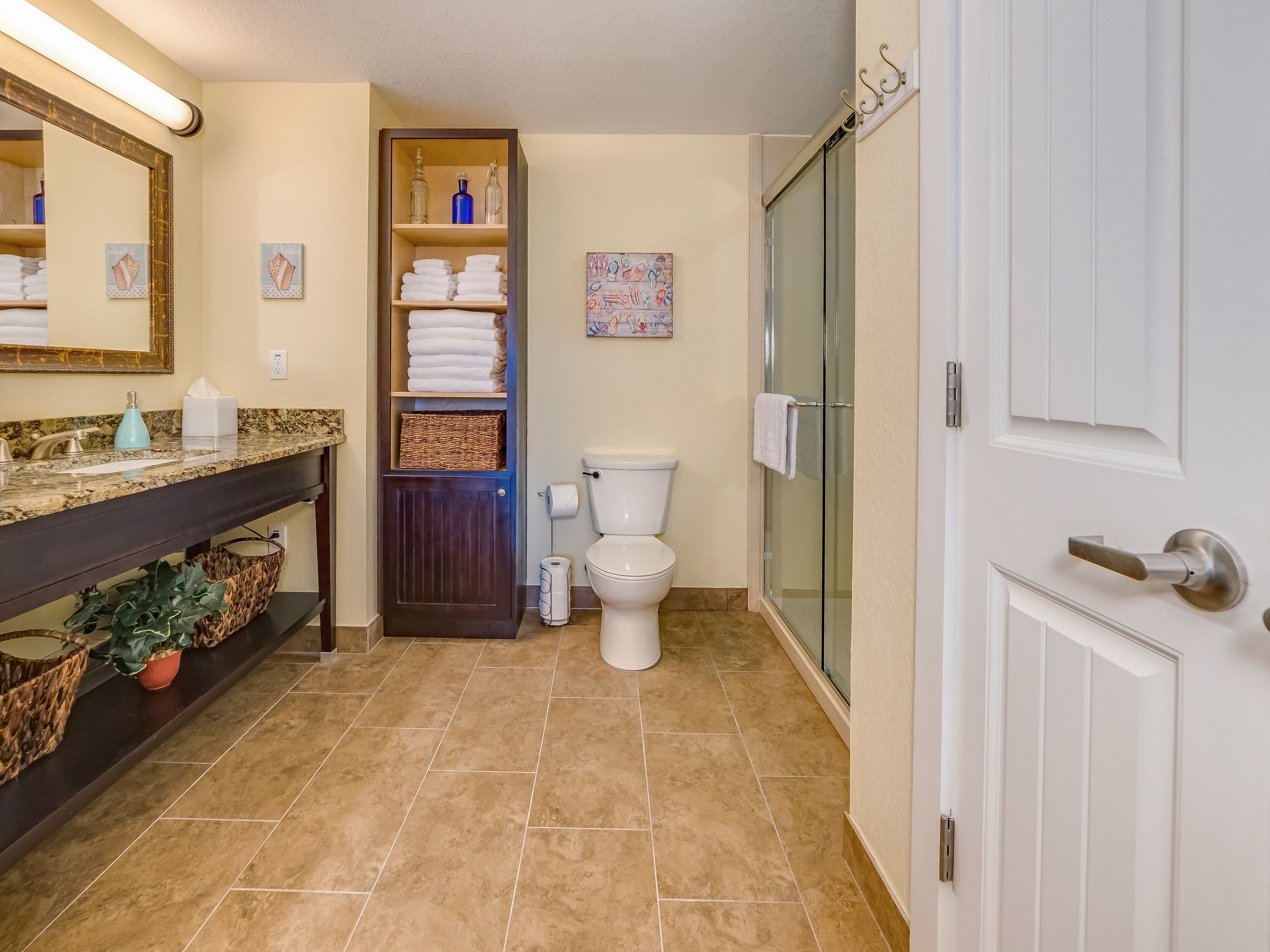 A bathroom with a marble countertop, a dark wooden vanity, a glass shower enclosure, and a toilet.