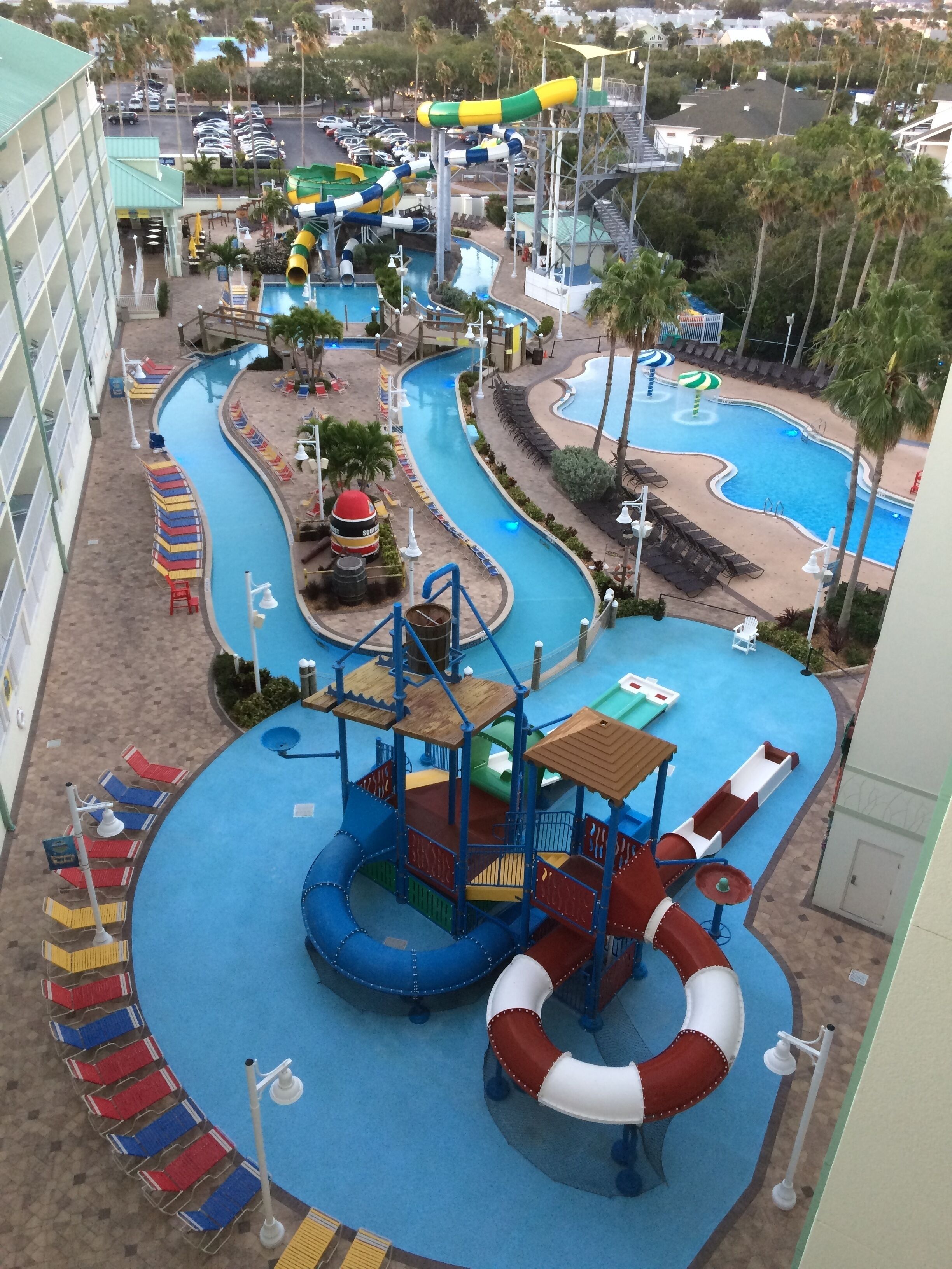 A water park with multiple slides and pools, surrounded by palm trees and a building with a poolside area.